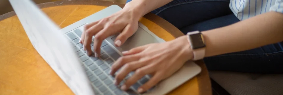 A woman typing on a laptop at a round wooden table
