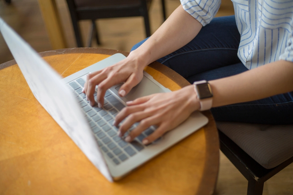 A woman typing on a laptop at a round wooden table