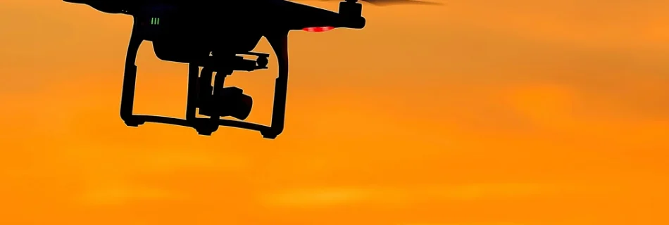 Silhouette of a camera drone flying against an orange sunset sky
