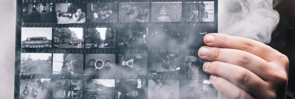 A hand holding a black and white contact sheet of photographs in swirling smoke