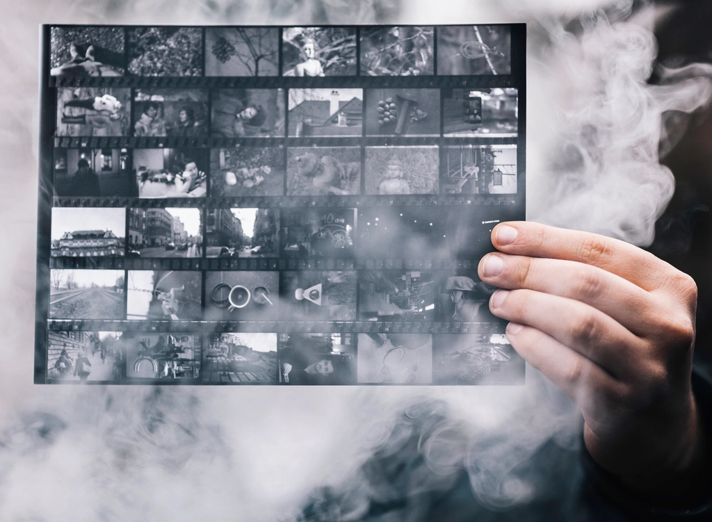 A hand holding a black and white contact sheet of photographs in swirling smoke